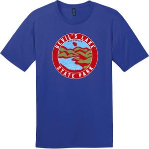 May include: A royal blue short-sleeve t-shirt featuring a circular graphic on the chest. The graphic depicts a landscape with green hills and a blue lake, topped with a small red map of Wisconsin and the text DEVIL'S LAKE STATE PARK in white.