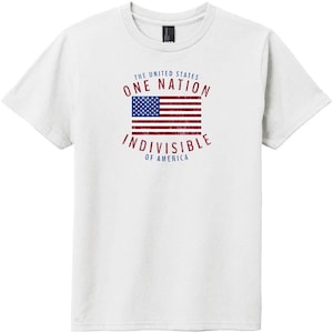 May include: A white short-sleeved t-shirt featuring a distressed graphic of the United States flag in the center. The text reads THE UNITED STATES ONE NATION INDIVISIBLE OF AMERICA in red and blue lettering arched around the flag graphic.