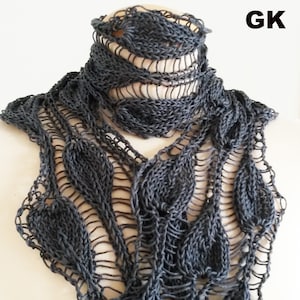 Könnte beinhalten: Ein grauer Strick Schal mit einem Blatt Muster. Der Schal ist aus einem zarten Garn gefertigt und hat einen Spitzenlook. Der Schal ist über den Hals einer Schaufensterpuppe gelegt.