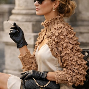 May include: A woman wearing a black beret and sunglasses, holding a cigarette. She is wearing a tan knitted shrug over a white dress, and carrying a black quilted handbag with a gold chain strap.