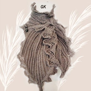 May include: A brown knitted shawl with a ruffled design. The shawl is draped over a mannequin and has a label that says "GK".