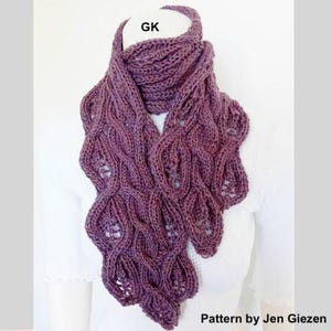 May include: A knitted scarf in a deep purple hue, featuring a textured, openwork design. The scarf has a flowing, leaf-like pattern and is draped around a white surface. The text "GK" is visible at the top, and "Pattern by Jen Giezen" is at the bottom.