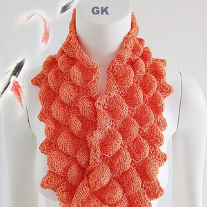 Peut inclure: Un col roulé en tricot orange vif avec un motif texturé en forme de bulles. Le col roulé est présenté sur un mannequin blanc.
