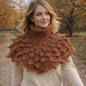 May include: A brown knitted cowl with a textured, layered design. The cowl has a high neck and a scalloped edge, creating a unique, textured appearance. The color is a warm, earthy brown, suitable for fall or winter wear.