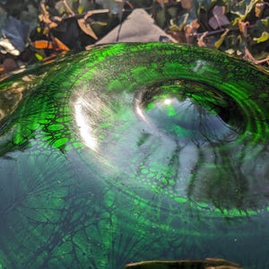 May include: Close-up of a decorative glass object with a swirling green and black pattern. The glass has a glossy finish and a textured surface, with a dark green base and lighter green highlights. The object's shape is rounded.