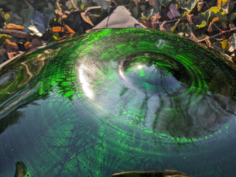 May include: Close-up of a decorative glass object with a swirling green and black pattern. The glass has a glossy finish and a textured surface, with a dark green base and lighter green highlights. The object's shape is rounded.