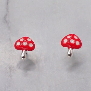 May include: A pair of silver mushroom earrings with red and white enamel. The mushrooms have white dots on the red caps.
