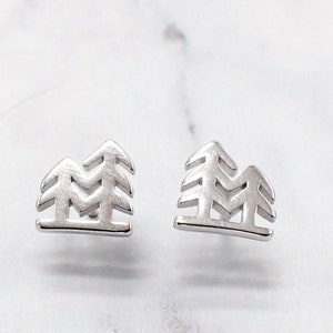 May include: A pair of silver earrings featuring a minimalist design of two stylized pine trees.