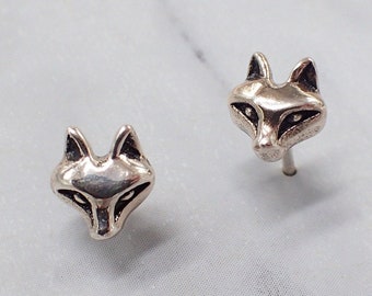Könnte beinhalten: Ein Paar silberne Ohrstecker in Form von Fuchs-Köpfen. Die Fuchs-Köpfe sind nach vorne gerichtet und haben schwarze Augen und eine detaillierte Schnauze.