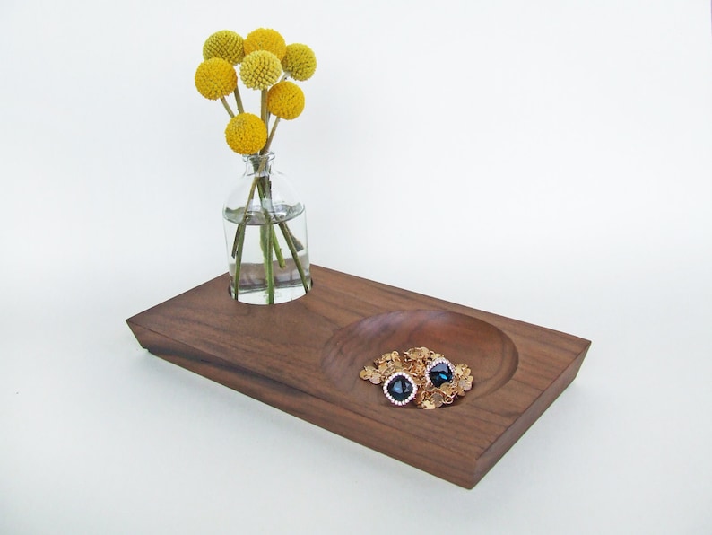 May include: A wooden tray with a small, round bowl and a cut-out for a vase. The bowl contains gold-colored jewelry and the vase holds a bouquet of yellow billy balls.