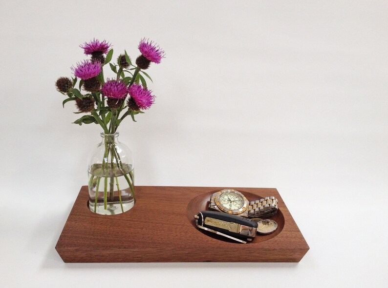 May include: A wooden tray with two compartments. One compartment holds a glass vase with a bouquet of purple thistle flowers. The other compartment holds a watch and a small pocket knife.