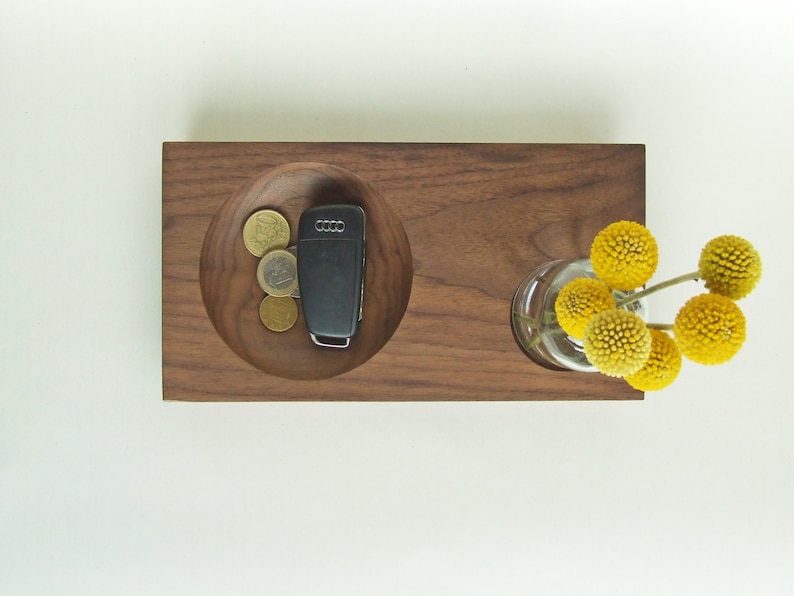 May include: A wooden tray with a round indentation for holding keys and coins. The tray also has a small vase for holding a bouquet of yellow flowers.