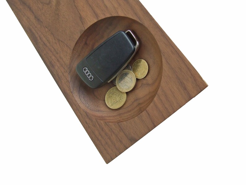 May include: A wooden tray with a circular indentation, holding a car key and a few coins. The tray is made of dark brown wood with a natural grain pattern.