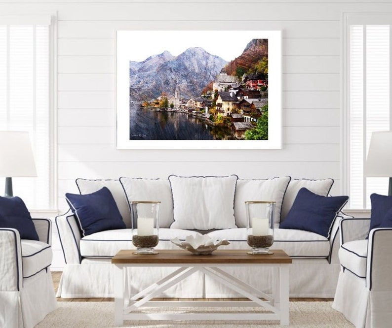 Peut inclure: Une photographie encadr&eacute;e d'un village pittoresque nich&eacute; dans une vall&eacute;e, entour&eacute; de montagnes enneig&eacute;es et d'un lac tranquille. Le village pr&eacute;sente des maisons color&eacute;es aux toits rouges et un clocher d'&eacute;glise.