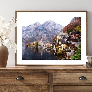 Peut inclure: Une peinture &agrave; l'aquarelle d'un petit village nich&eacute; dans une vall&eacute;e de montagne. Le village est entour&eacute; de montagnes enneig&eacute;es et d'un lac. Les maisons sont peintes de couleurs vives et ont des toits rouges. La peinture est encadr&eacute;e dans un cadre en bois brun.