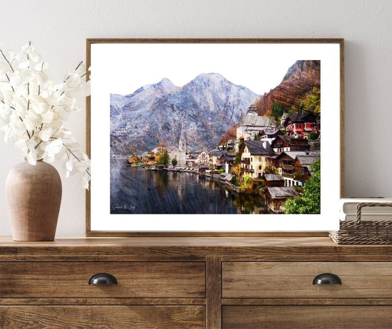 Peut inclure: Une peinture &agrave; l'aquarelle d'un petit village nich&eacute; dans une vall&eacute;e de montagne. Le village est entour&eacute; de montagnes enneig&eacute;es et d'un lac. Les maisons sont peintes de couleurs vives et ont des toits rouges. La peinture est encadr&eacute;e dans un cadre en bois brun.