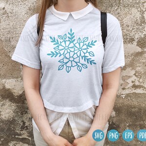 Op de afbeelding: Een wit T-shirt met een blauw bloemenontwerp. Het ontwerp toont gestileerde bloemen met meerdere bloemblaadjes en bladeren.