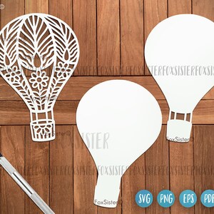 May include: Three white paper cut-out hot air balloons. One balloon has a detailed floral design. The balloons are on a wood background.