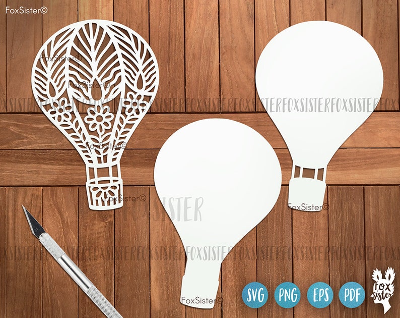 May include: Three white paper cut-out hot air balloons. One balloon has a detailed floral design. The balloons are on a wood background.