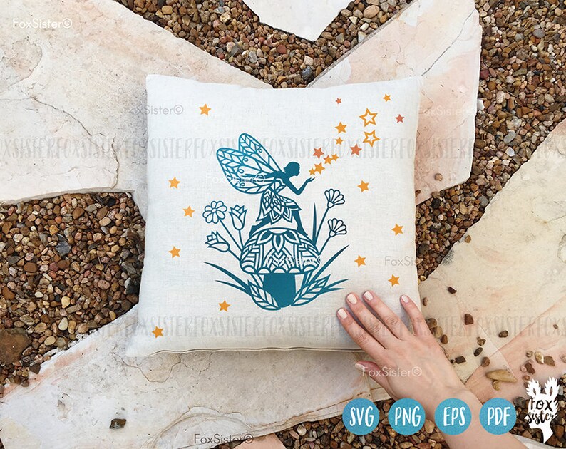 May include: A white pillow with a blue and teal silhouette of a fairy sitting on a mushroom with stars and flowers around it.