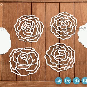 May include: Five white paper cutouts of roses on a wooden background. The roses are layered and have a delicate, intricate design. The cutouts are ideal for crafting and decorating.