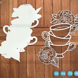 May include: White silhouette of three stacked teacups with floral designs, on a wooden background. The teacups are decorated with flowers and leaves.