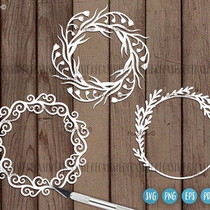May include: Three white decorative wreaths with intricate floral designs. The wreaths are cut from paper and are perfect for crafting projects.