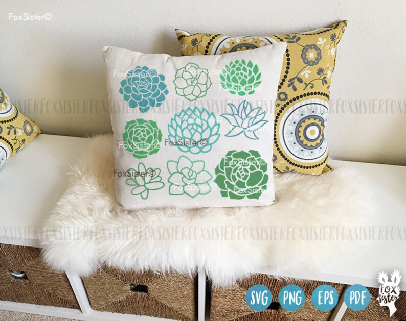 May include: A white pillow with a green and blue succulent design. The pillow has the text "FoxSister" on it. The pillow is sitting on a white faux fur throw.
