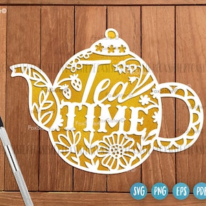 Op de afbeelding: Een wit silhouet van een theepot met bloemmotieven en de tekst "Tea Time" in goud. De theepot staat op een houten achtergrond.