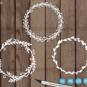 May include: Three white, decorative, paper wreaths with intricate designs. The wreaths are on a wood background.