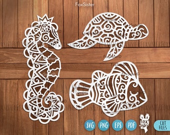Könnte beinhalten: Drei weiße, filigrane, lasergeschnittene Designs eines Seepferds, einer Schildkröte und eines Fisches. Die Designs sind auf einem Holzgrund.