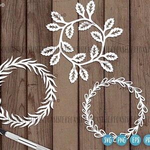 May include: Three white paper cut-out wreaths with a leafy design. The wreaths are on a wood background. The words "SVG PNG EPS PDF" are at the bottom of the image.