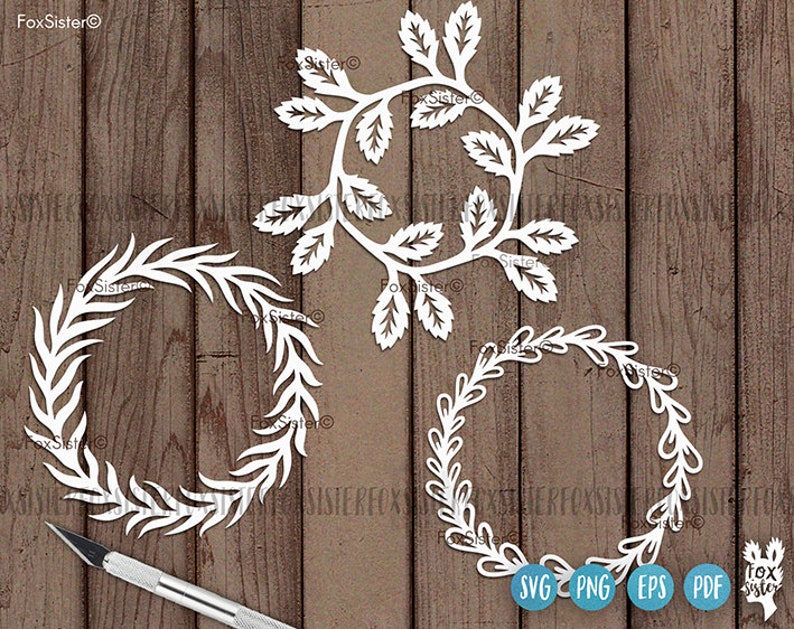 May include: Three white paper cut-out wreaths with a leafy design. The wreaths are on a wood background. The words "SVG PNG EPS PDF" are at the bottom of the image.