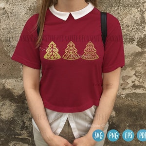 May include: A red short-sleeved shirt with a white collar features three gold Christmas tree designs. The trees are stylized and have a decorative, intricate pattern. The shirt is worn by a person standing in front of a textured wall.