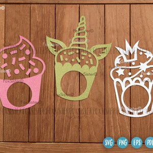 May include: Three glittery cupcake-shaped cutouts in pink, green, and white. The pink cupcake has sprinkles, the green one has a unicorn horn, and the white one has a crown. Each has a circular opening. The FoxSister logo is visible.