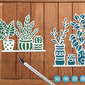 May include: SVG cut file design of three potted plants. The plants are a cactus, a leafy plant, and a fern. The pots are white with a teal design. The design is on a wood background.