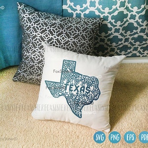 May include: A white square pillow with a teal Texas outline filled with floral patterns and the word "TEXAS". Other pillows in the background are teal and gray with geometric patterns. The pillow is on a beige carpet.