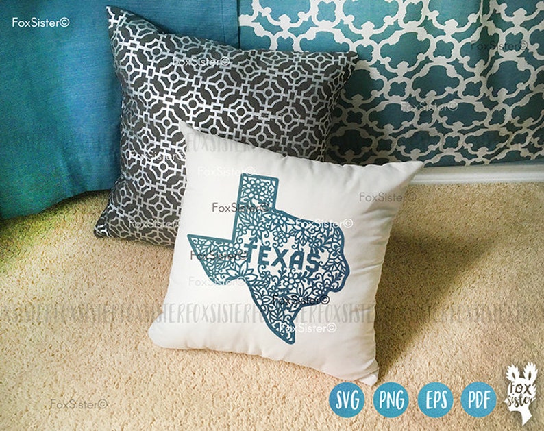 May include: A white square pillow with a teal Texas outline filled with floral patterns and the word "TEXAS". Other pillows in the background are teal and gray with geometric patterns. The pillow is on a beige carpet.