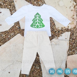 May include: A white long-sleeved shirt with a green Christmas tree design on the front. The shirt is paired with beige pants. The image includes the text "FoxSister" and the file formats "SVG", "PNG", "EPS", and "PDF".