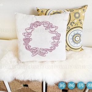 May include: A white pillow with a pink design of teacups in a circle. The teacups are arranged in a circle with a swirl design in the center. The pillow is on a white fluffy surface.