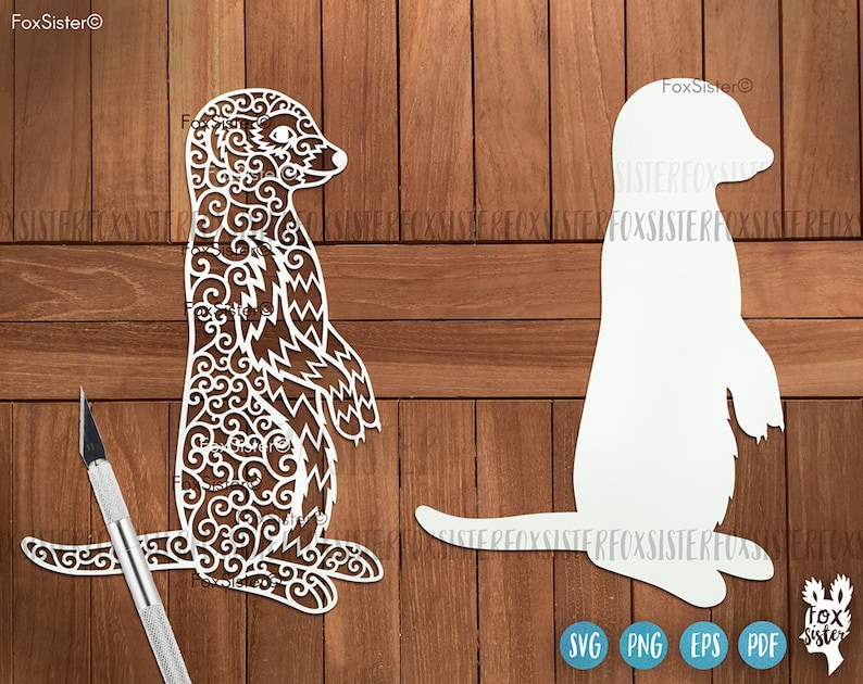 May include: A white silhouette and a detailed, intricate cutout of a meerkat standing on its hind legs with its arms raised. The meerkat is facing to the right. The background is a wood grain pattern.