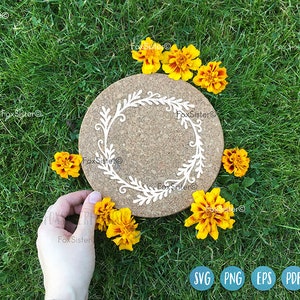 May include: A cork coaster with a white floral design, surrounded by yellow flowers on a green grassy background.