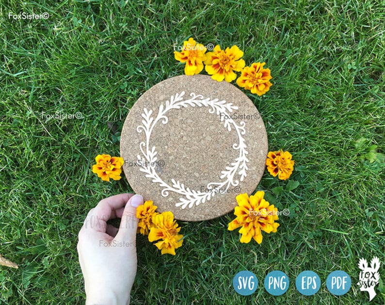May include: A cork coaster with a white floral design, surrounded by yellow flowers on a green grassy background.
