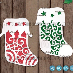 May include: Two white stocking cutouts with intricate designs. One stocking has a red and white design with stars and swirls. The other stocking has a green and white design with swirls. The stockings are on a wood background.