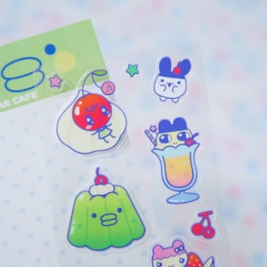 May include: A sheet of clear stickers featuring cute cartoon food and character designs. The stickers include a cherry character, a green jelly, a drink, and other colorful illustrations. The sheet also has a green card with the text "AR CAFE".
