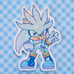 May include: A holographic sticker featuring Silver the Hedgehog from the Sonic the Hedgehog video game series. The sticker has a light blue color scheme with silver glitter accents. Silver is depicted in a dynamic pose, giving a peace sign.