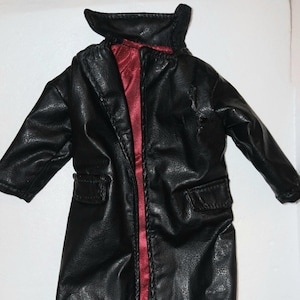 May include: A black long-sleeved coat with a textured finish, featuring a high collar, two front pockets with flaps, and a vibrant red satin-like lining visible along the open front placket. The garment is designed with a structured silhouette.