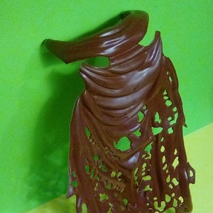 May include: A brown, tattered, plastic cape with a jagged edge. The cape is made to look like it is ripped and torn.