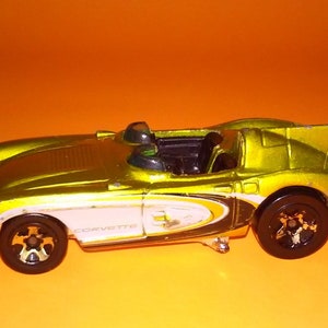 May include: A yellow toy car with a white stripe and the word "Corvette" on the side. The car has black wheels and a black interior.