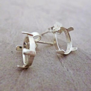Puede incluir: Un par de monturas para pendientes de plata con garras ovaladas diseñadas para sujetar piedras preciosas. Cada montura incluye un poste y una estructura metálica con cuatro garras que se extienden hacia arriba.